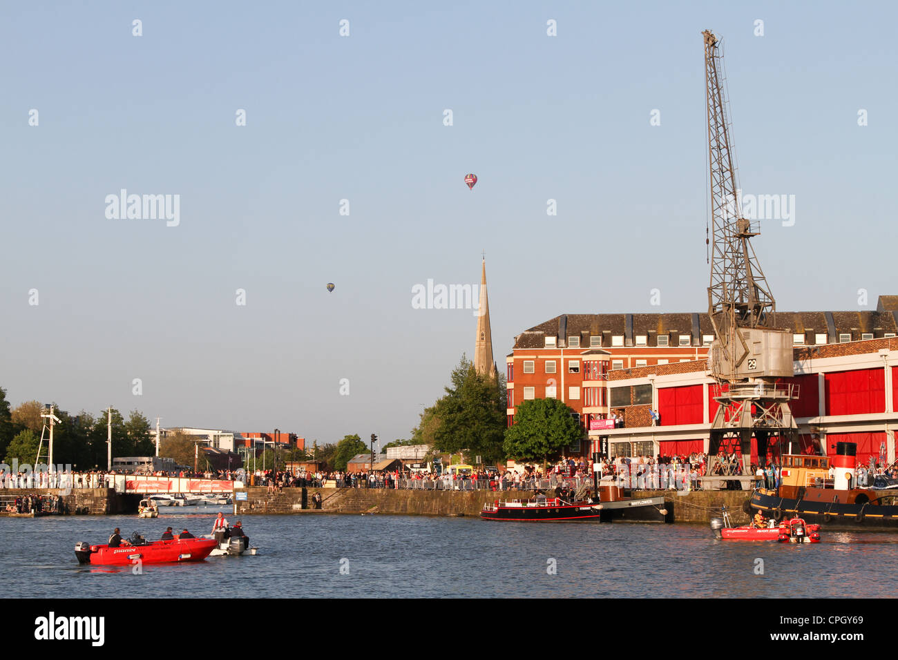 Linea di folle Bristol Docks waterfront, da M gru sparso nel sole pomeridiano, St Mary Redcliffe guglia e palloncini in background Foto Stock