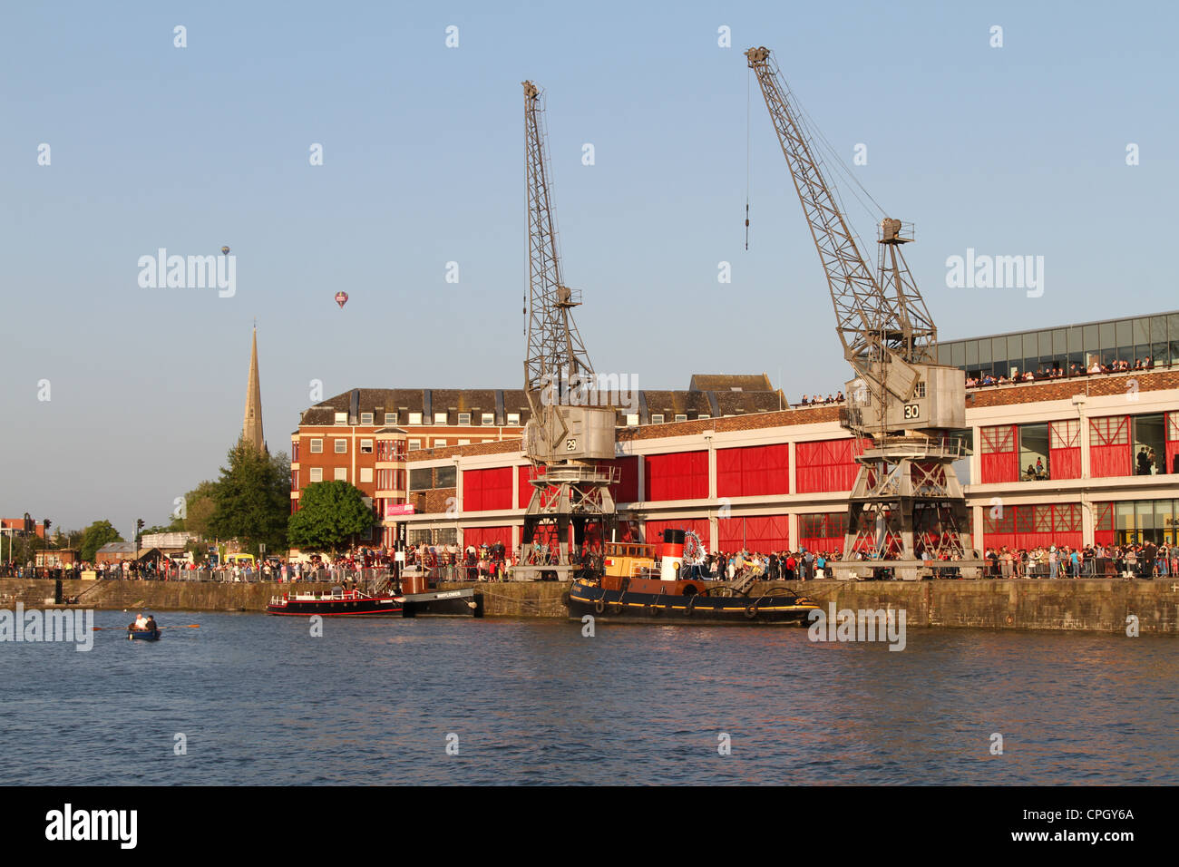 Linea di folle Bristol Docks waterfront, da M gru sparso nel sole pomeridiano, St Mary Redcliffe guglia e palloncini in background Foto Stock