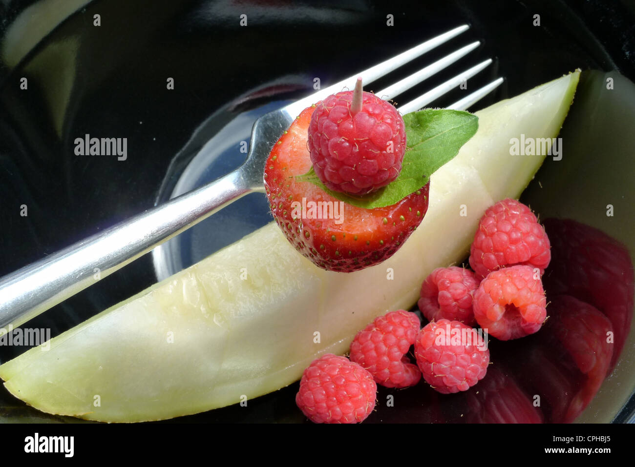 Una fragola, lampone e un pezzo di melone come un Hors d' oeuvres, su una piastra nera con argento forcella. Foto Stock