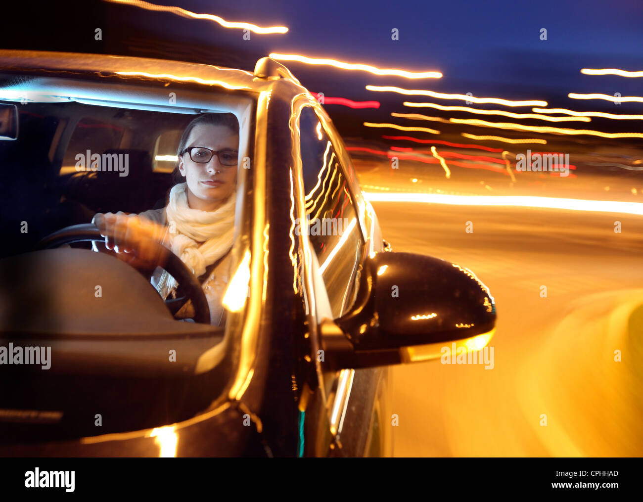 Giovane donna è alla guida di una macchina di notte, attraverso una città, illuminato con lampioni. Foto Stock