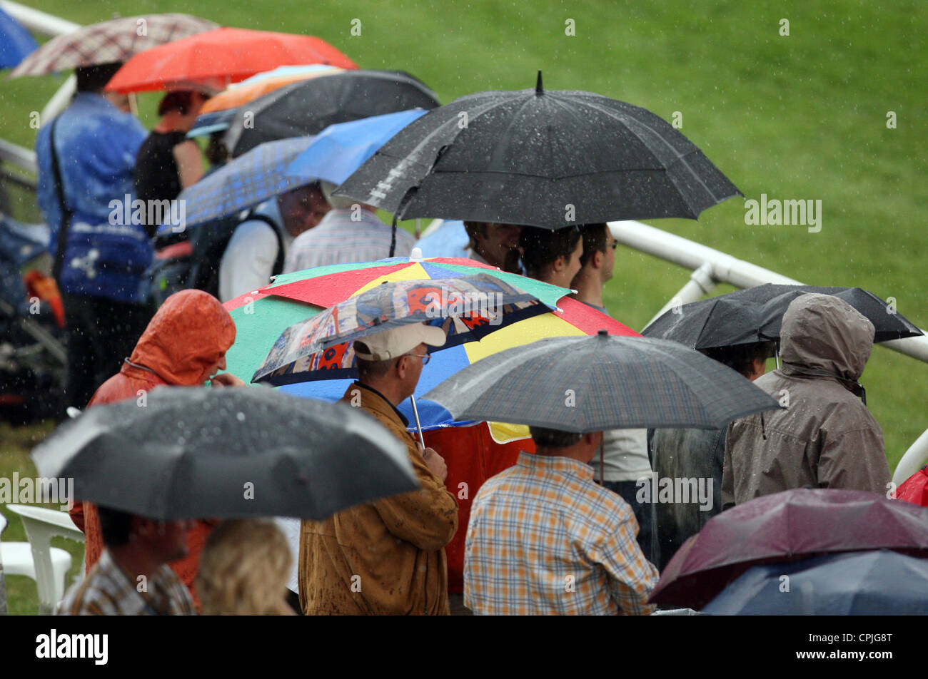 Persone a corse di cavalli che si nasconde sotto gli ombrelloni durante la pioggia, Amburgo, Germania Foto Stock