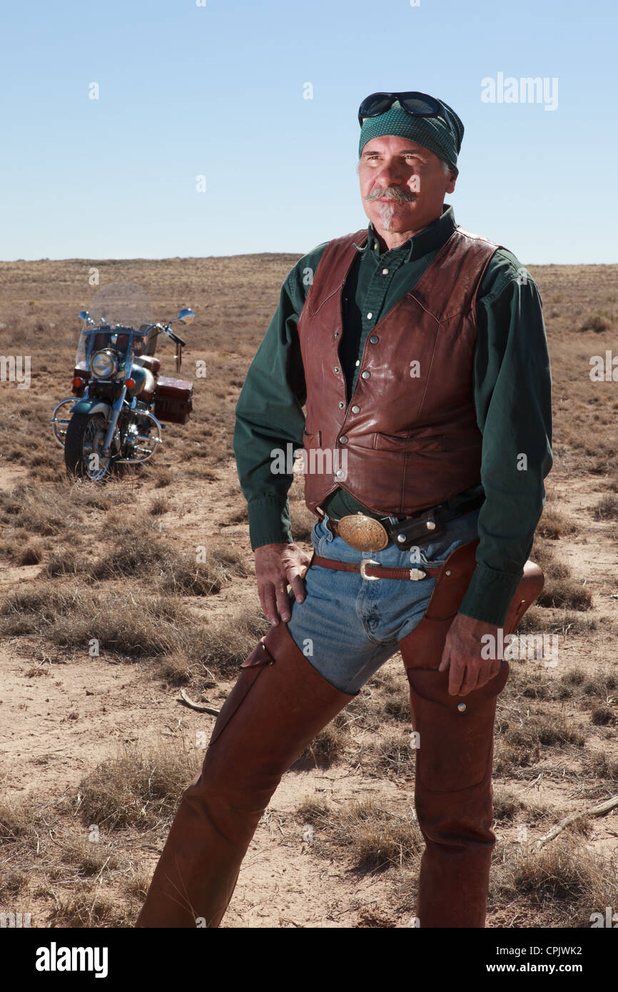 Vecchio uomo caucasico indossa in cuoio marrone in piedi accanto alla sua moto nel deserto. Foto Stock