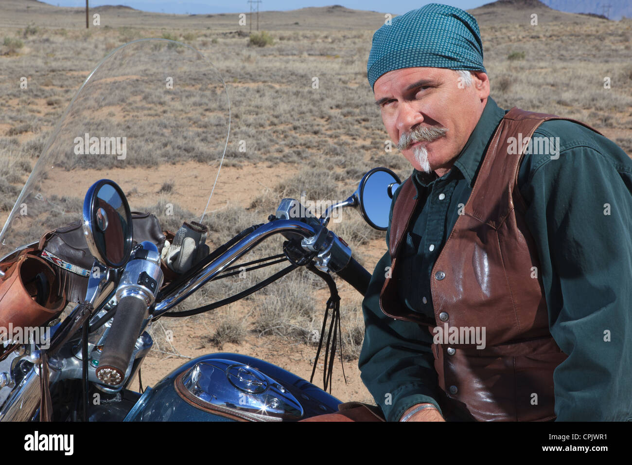 Vecchio uomo caucasico indossa in cuoio marrone in piedi accanto alla sua moto nel deserto. Foto Stock