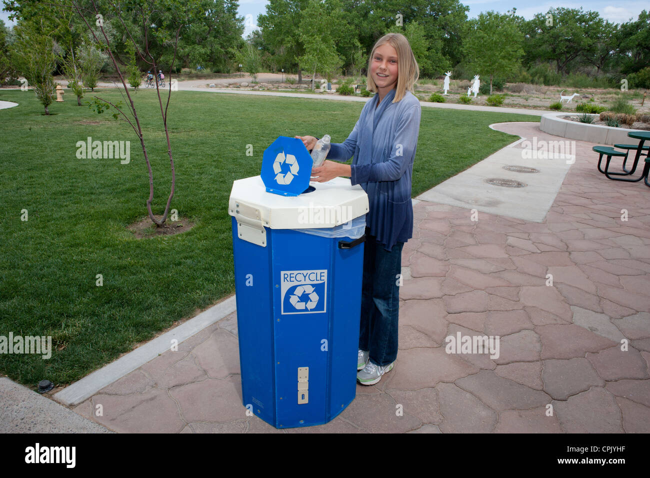 Ragazza di dodici anni mettendo un vuoto che la bottiglia di plastica in un contenitore di riciclaggio all'esterno. Foto Stock
