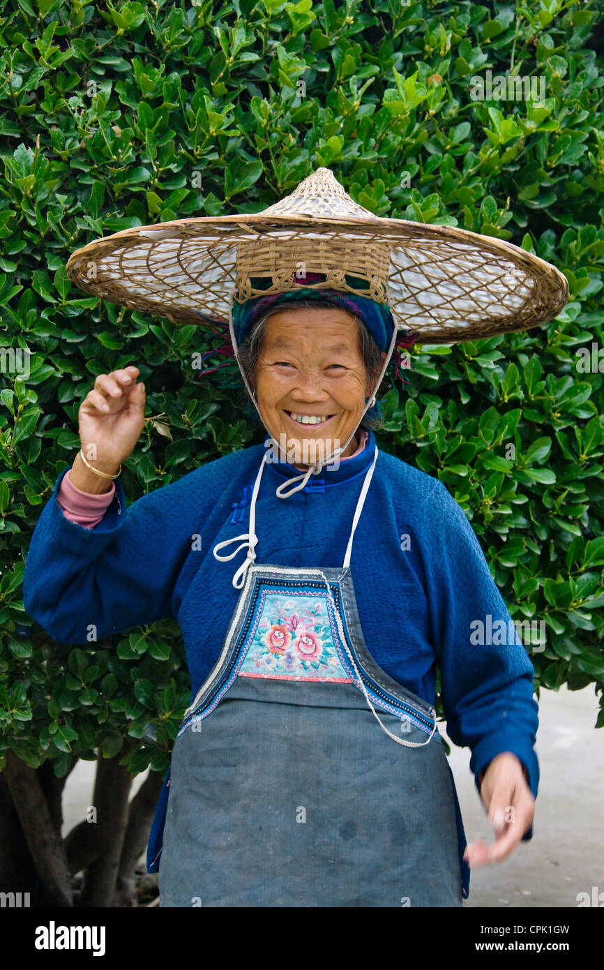 Anziani Xijia donna in costume tradizionale con bambù hat, Shilongzhai, vicino a Kaili, Guizhou, Cina Foto Stock