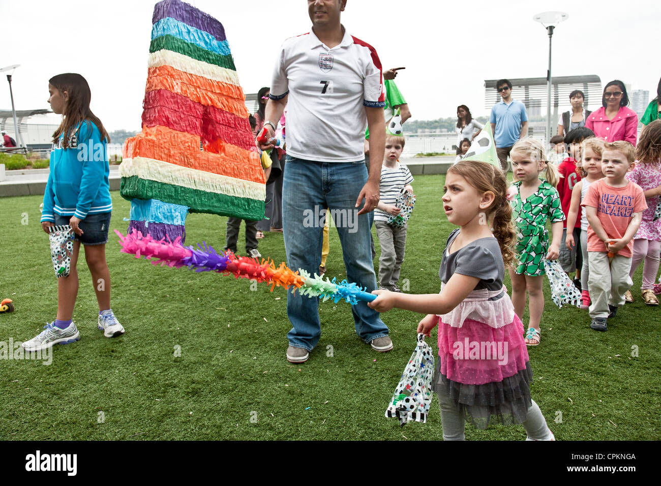 Bambina abito partito esce swinging contro arcobaleno colorato 4 bersaglio come altri 4 anni di attendere il loro turno festa di compleanno Foto Stock