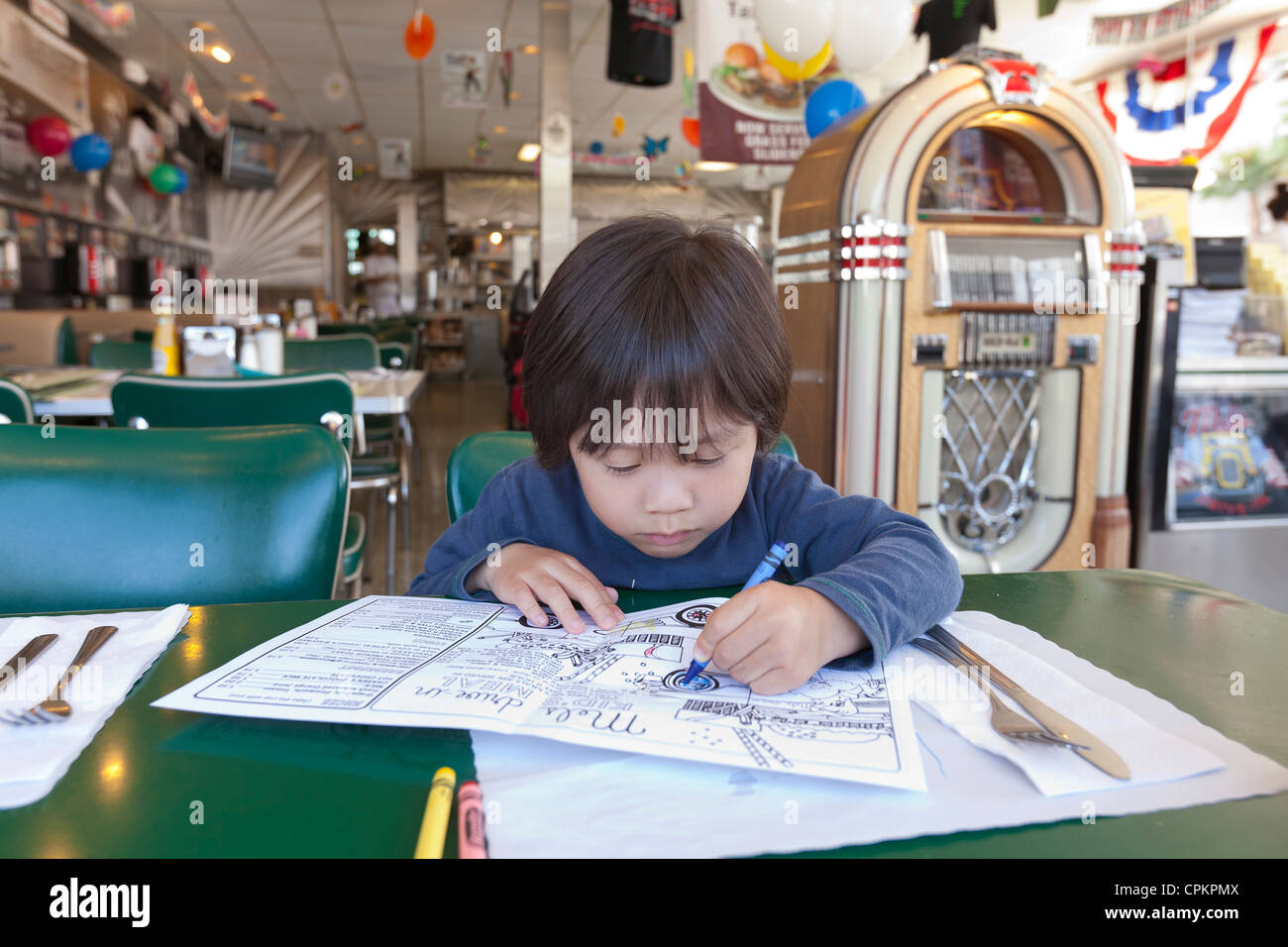 Un giovane ragazzo asiatico la colorazione di un bambini's Diner menu Foto Stock