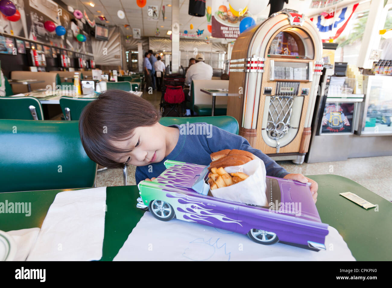 Un piccolo ragazzo asiatico guardando un modello di auto piatto da portata in un diner Foto Stock