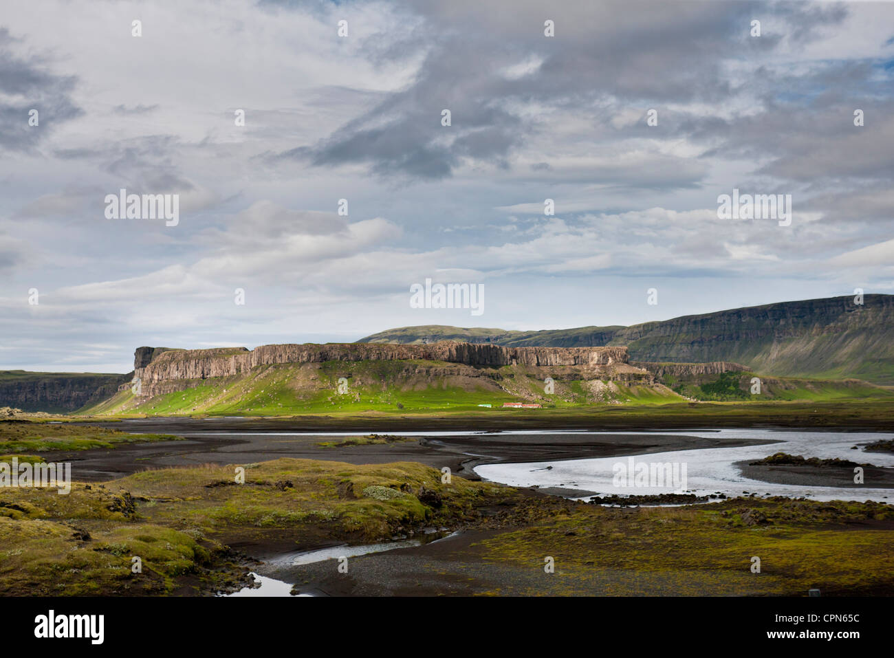 L'Islanda, stream in esecuzione attraverso il campo di lava, scogliere di basalto in distanza Foto Stock