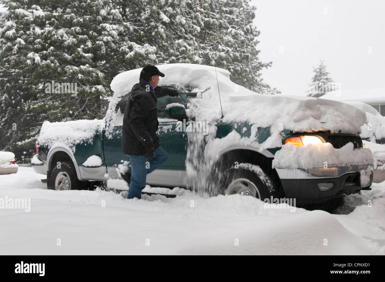 Un senior attivo maschio adulto sfridi neve fuori il suo carrello nel bel mezzo di una tempesta di neve in Olympia, Washington. Foto Stock