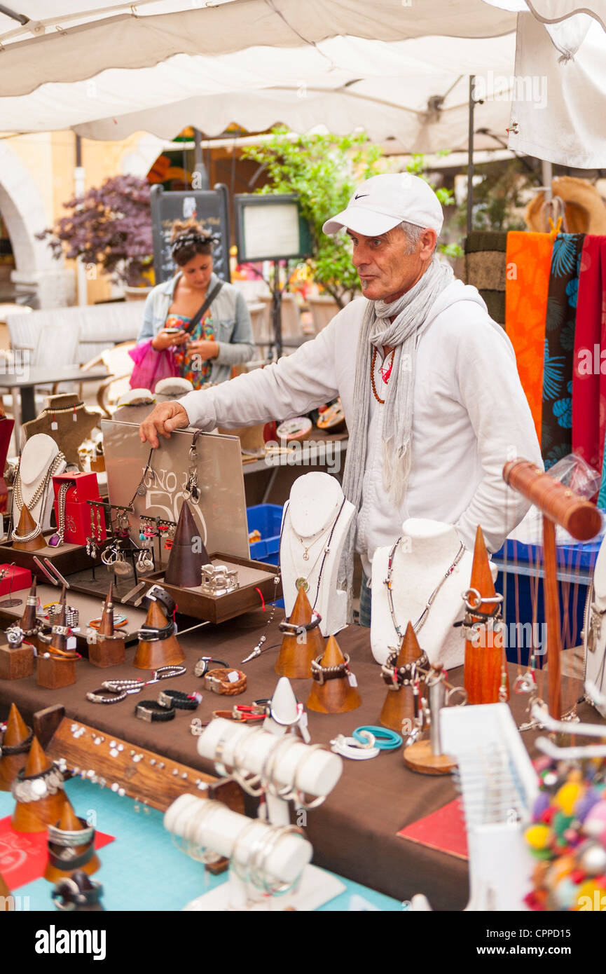 Il sud della Francia Provincia Valbonne mercato grigio grigio pelose anziano Uomo in camicia bianca t shirt berretto da baseball su articoli di bigiotteria Articoli di gioielleria di stallo del display Foto Stock