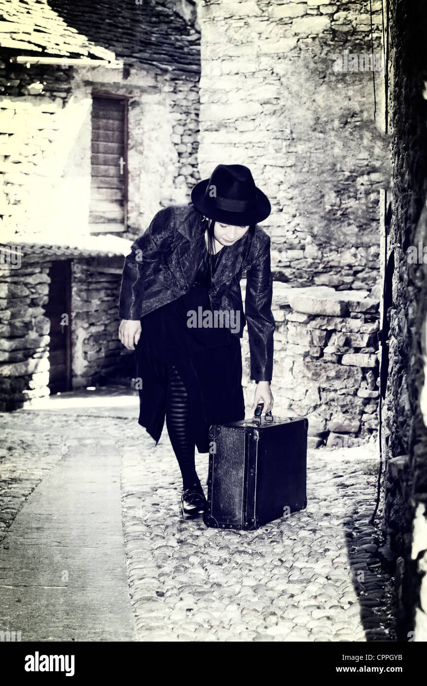 Giovane donna con cappello è a piedi attraverso una stradina con una vecchia valigia Foto Stock