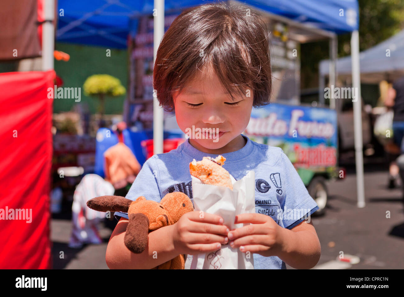 Giovane ragazzo asiatico di mangiare un dolce al mercato degli agricoltori - Stockton California USA Foto Stock