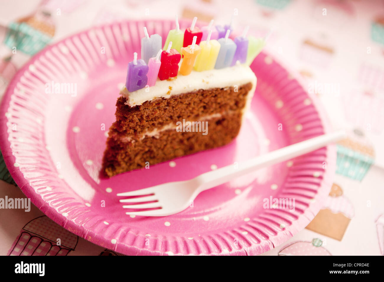 Una fetta di torta di compleanno con il "Buon compleanno" candele, impostato su una carta rosa piastra su una tortina sfondo modellato Foto Stock