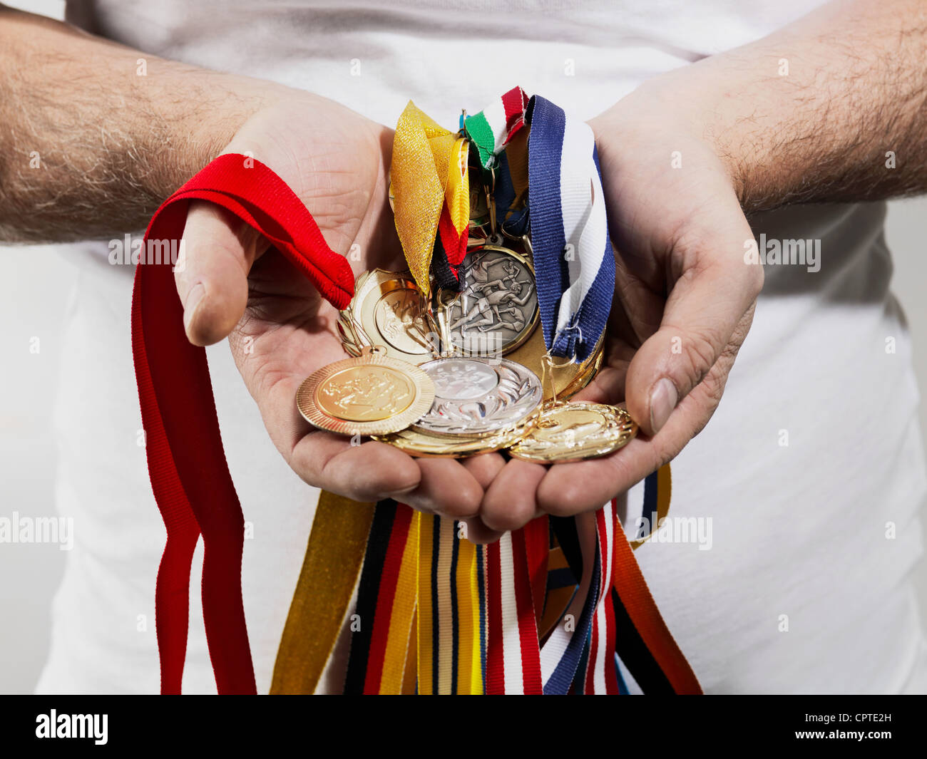 Uomo maturo holding medaglie d oro contro uno sfondo bianco Foto Stock