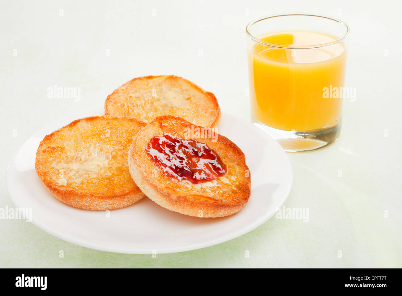 Burrosa, tostate muffin inglesi o cialdine con marmellata e un bicchiere di succo di arancia su uno sfondo verde chiaro. Foto Stock