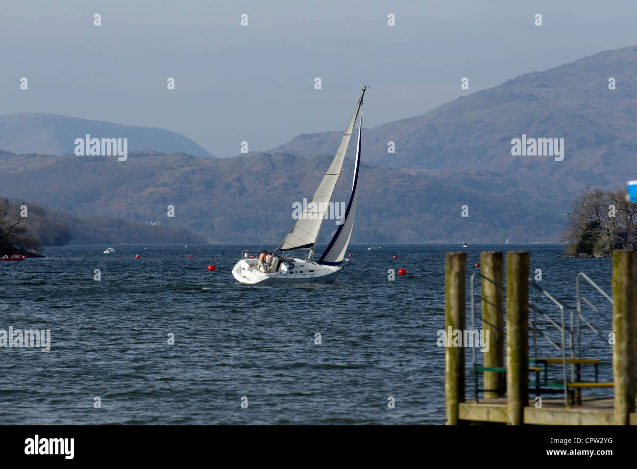 Yacht a pieno la vela in inverno sul lago di Windermere con le montagne e brughiere in background Foto Stock