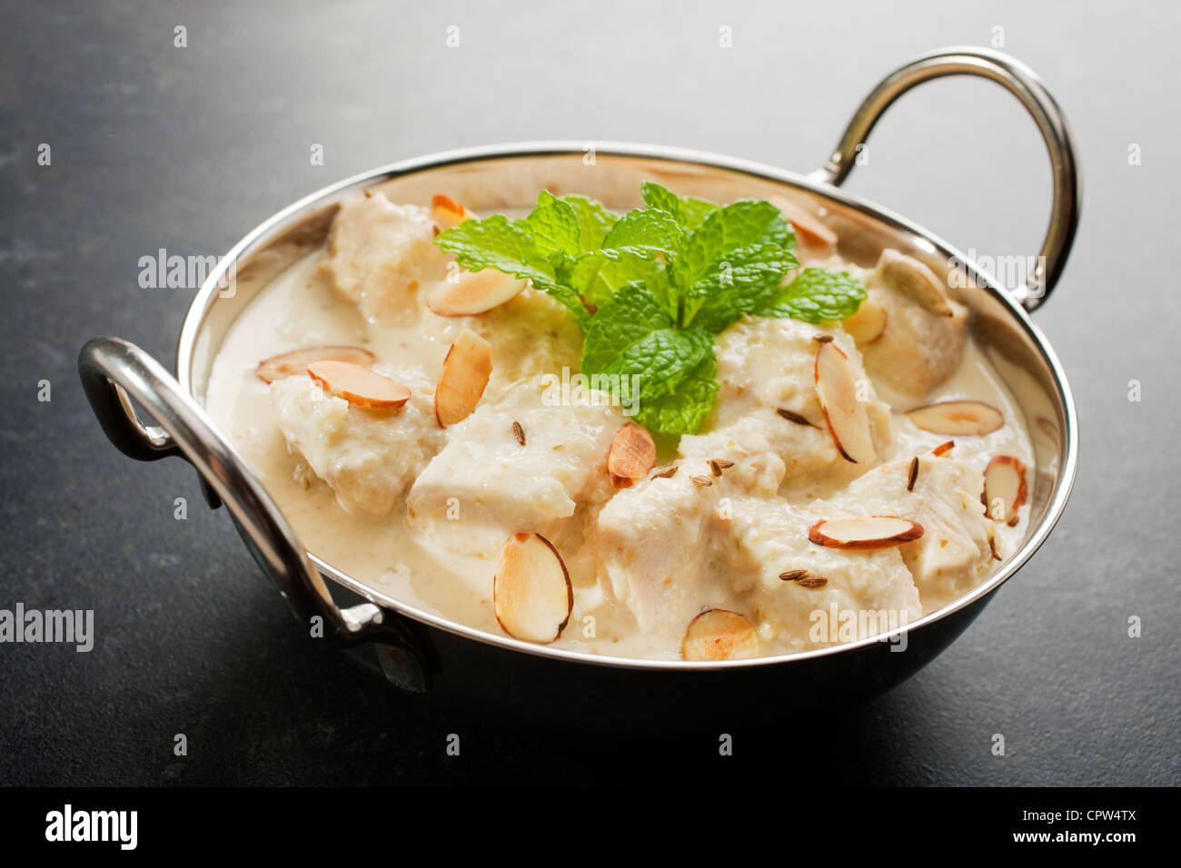 Dolce e cremoso korma di pollo in un piatto di Balti, guarnita con la menta, mandorle tostate e semi di cumino, su uno sfondo scuro. Foto Stock