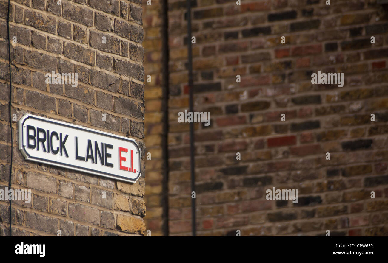 Brick Lane E1 strada segno su angolo di strada un muro di mattoni sfondo con parete a destra in ombra East End di Londra Inghilterra REGNO UNITO Foto Stock