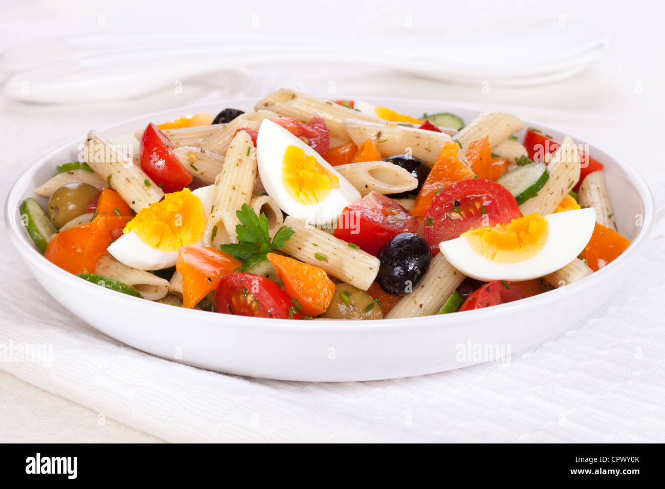 Una ciotola di insalata di pasta con uova, pomodori, cetrioli, arancio pepe e le olive in un condimento di erbe. Foto Stock
