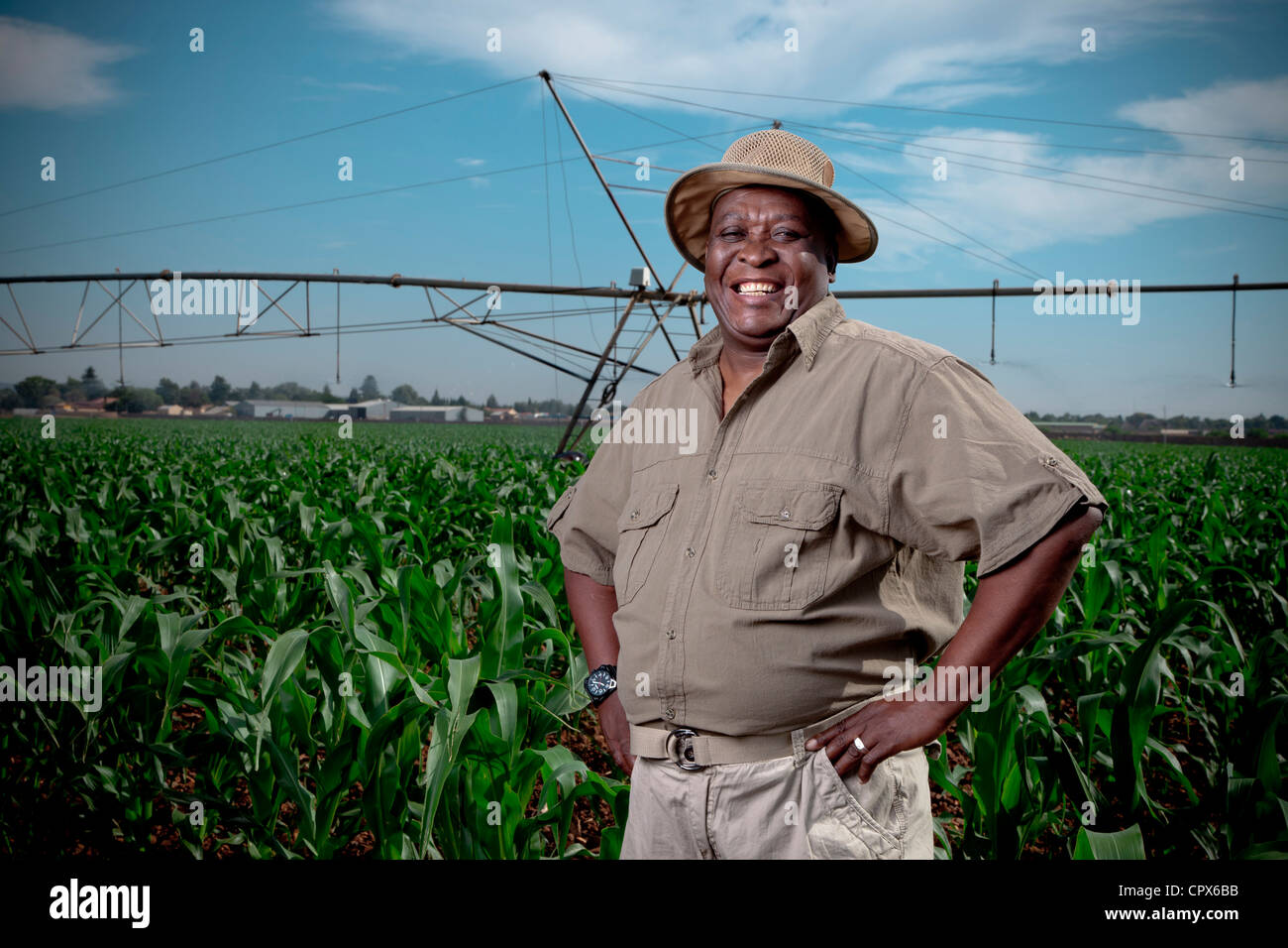 L'agricoltore nero sorge sorridente in un campo di coltivazione con sistemi di irrigazione in background Foto Stock L'agricoltore nero sorge sorridente in un campo di coltivazione con sistemi di irrigazione in background Foto Stock