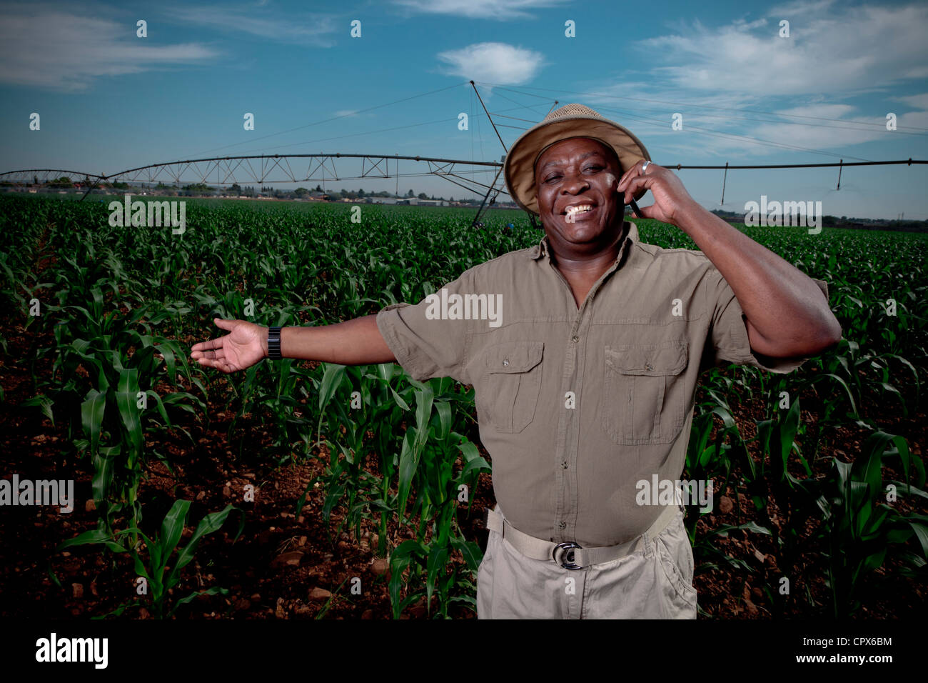 L'agricoltore nero sorge sorridente in un campo di coltivazione con sistemi di irrigazione in background Foto Stock L'agricoltore nero sorge sorridente in un campo di coltivazione con sistemi di irrigazione in background Foto Stock