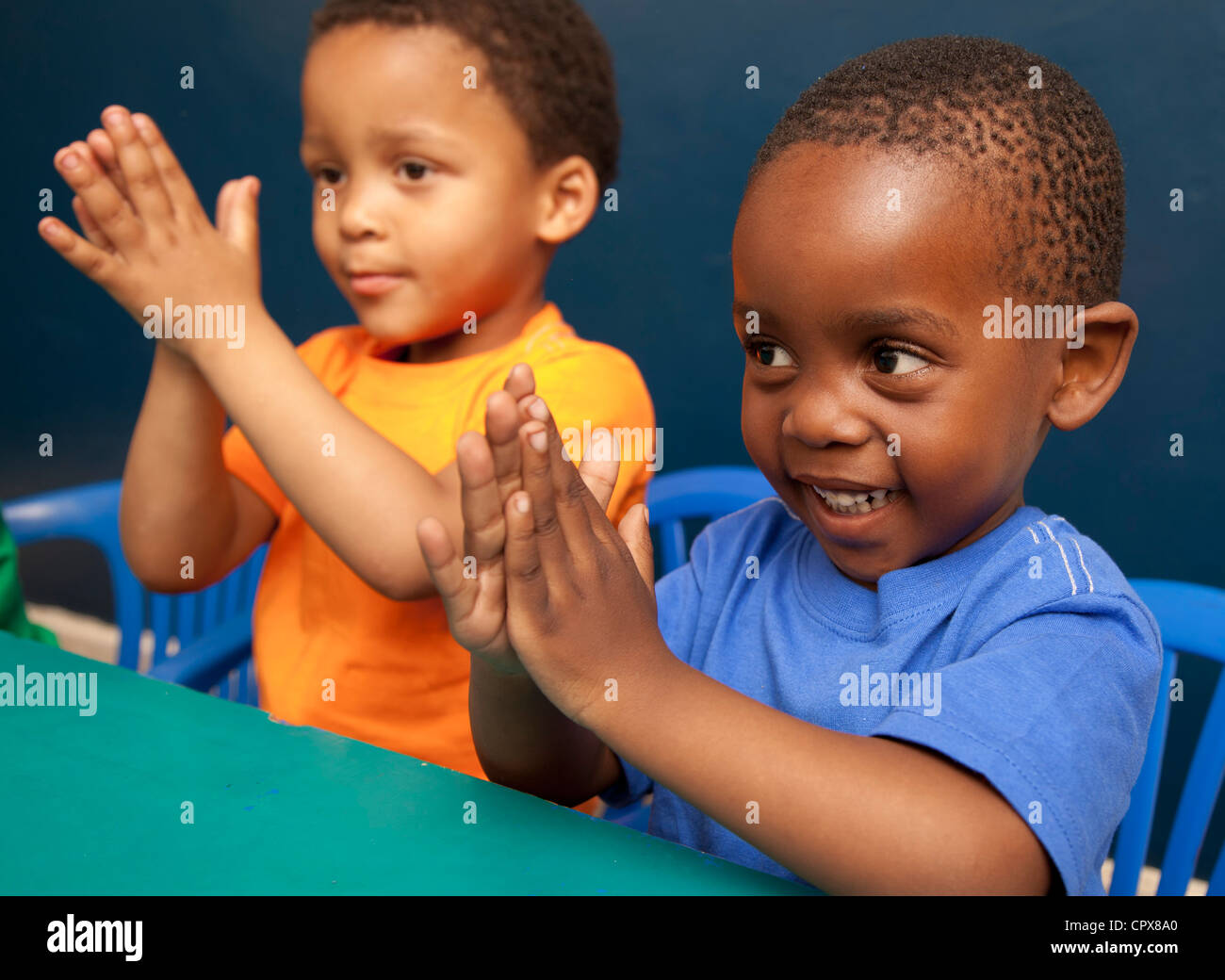 Due bambini seduti ad una scrivania battendo le mani Foto Stock