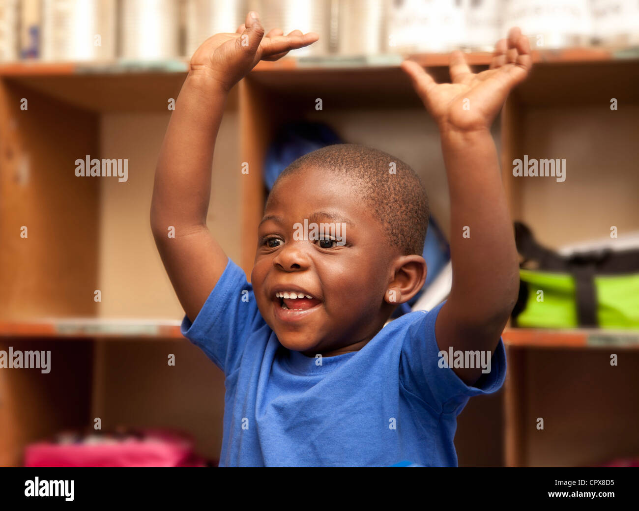 Bambino seduto alla scrivania con le mani in aria Foto Stock