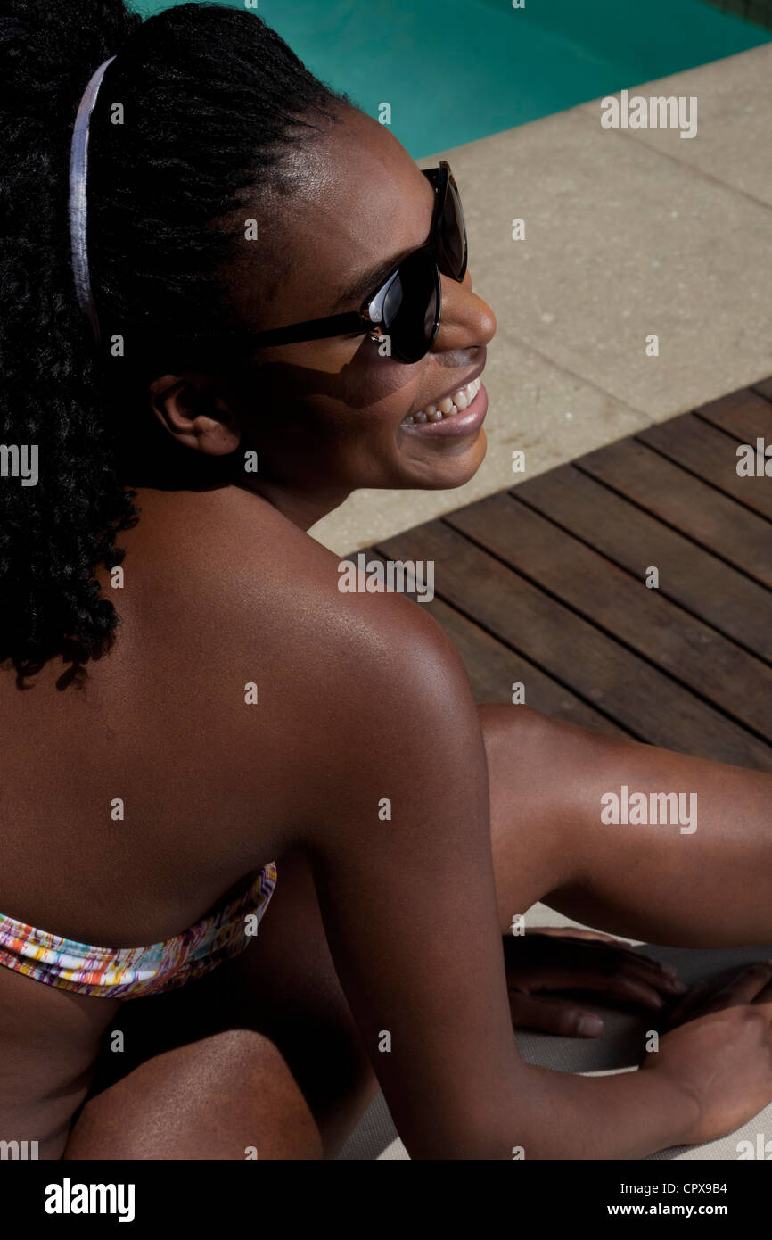 Giovane nero donna sdraiata su una sedia a sdraio di fianco alla piscina Foto Stock