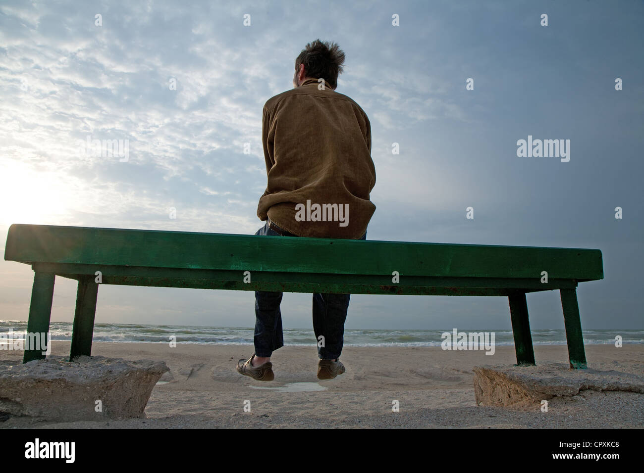 Adulto Uomo seduto da solo sul banco di lavoro guardando un mare tempestoso da soli Foto Stock