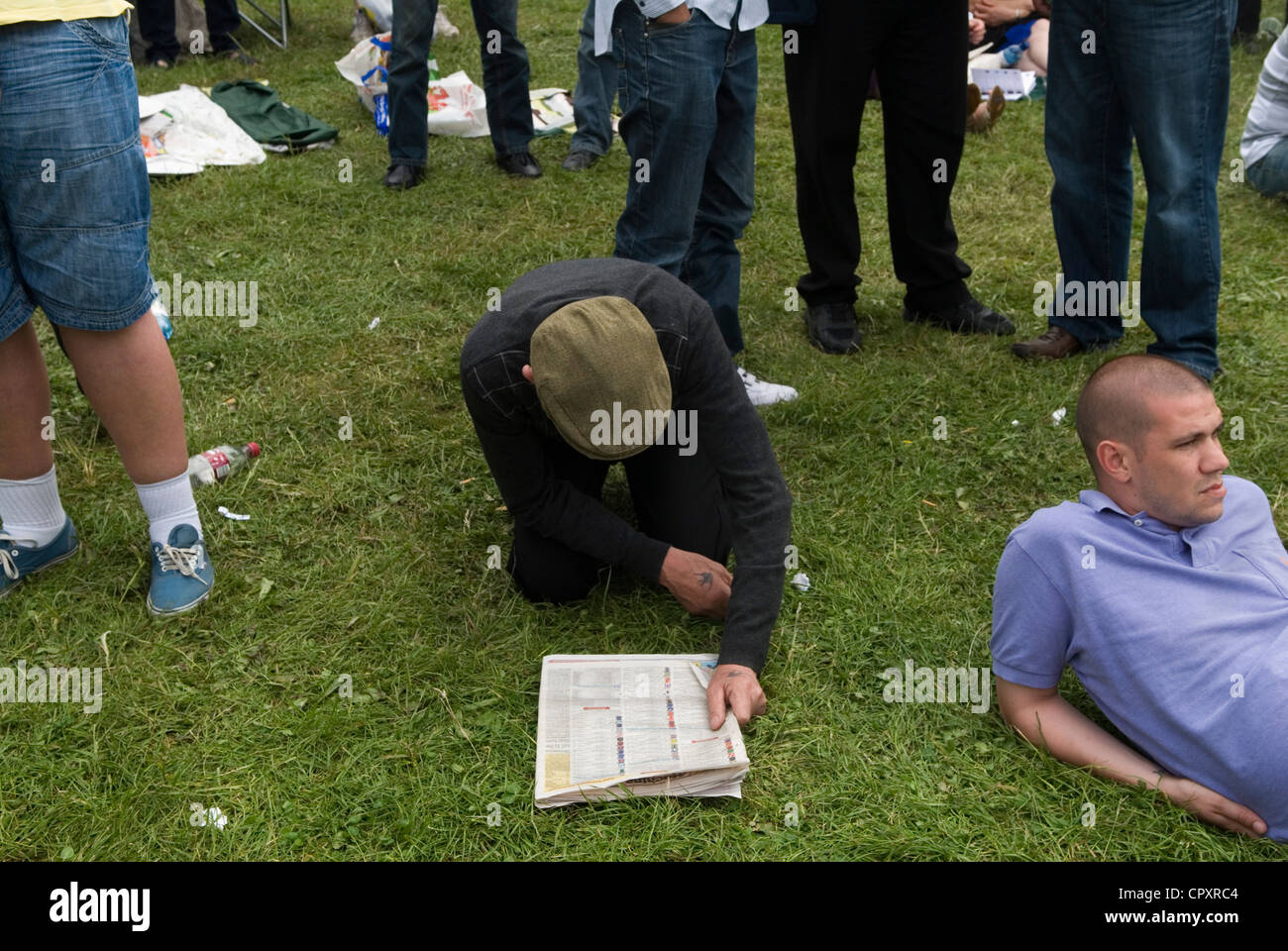 Uomo che indossa un berretto piatto a terra leggendo le pagine sportive di un giornale, sta controllando i corridori e le loro probabilità. Ha il tatuaggio di Swallow sulla mano, è un ex marinaio. Sono sulla collina, a guardare le corse di cavalli Derby Day, Epsom Downs Surrey UK 2012 2010s HOMER SYKES Foto Stock