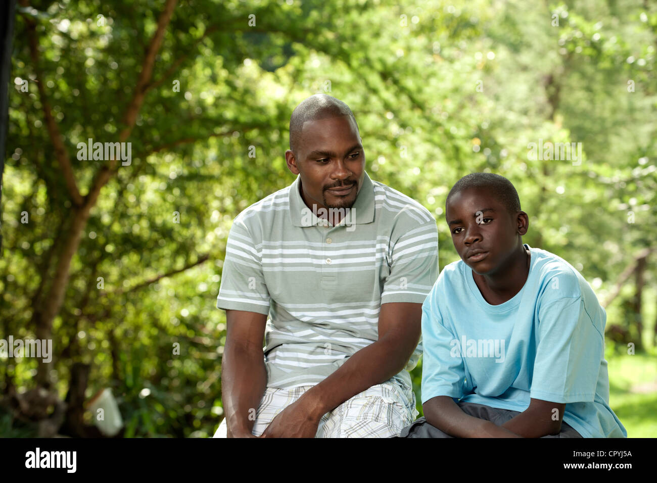 African padre e figlio seduti fuori in un giardino Foto Stock