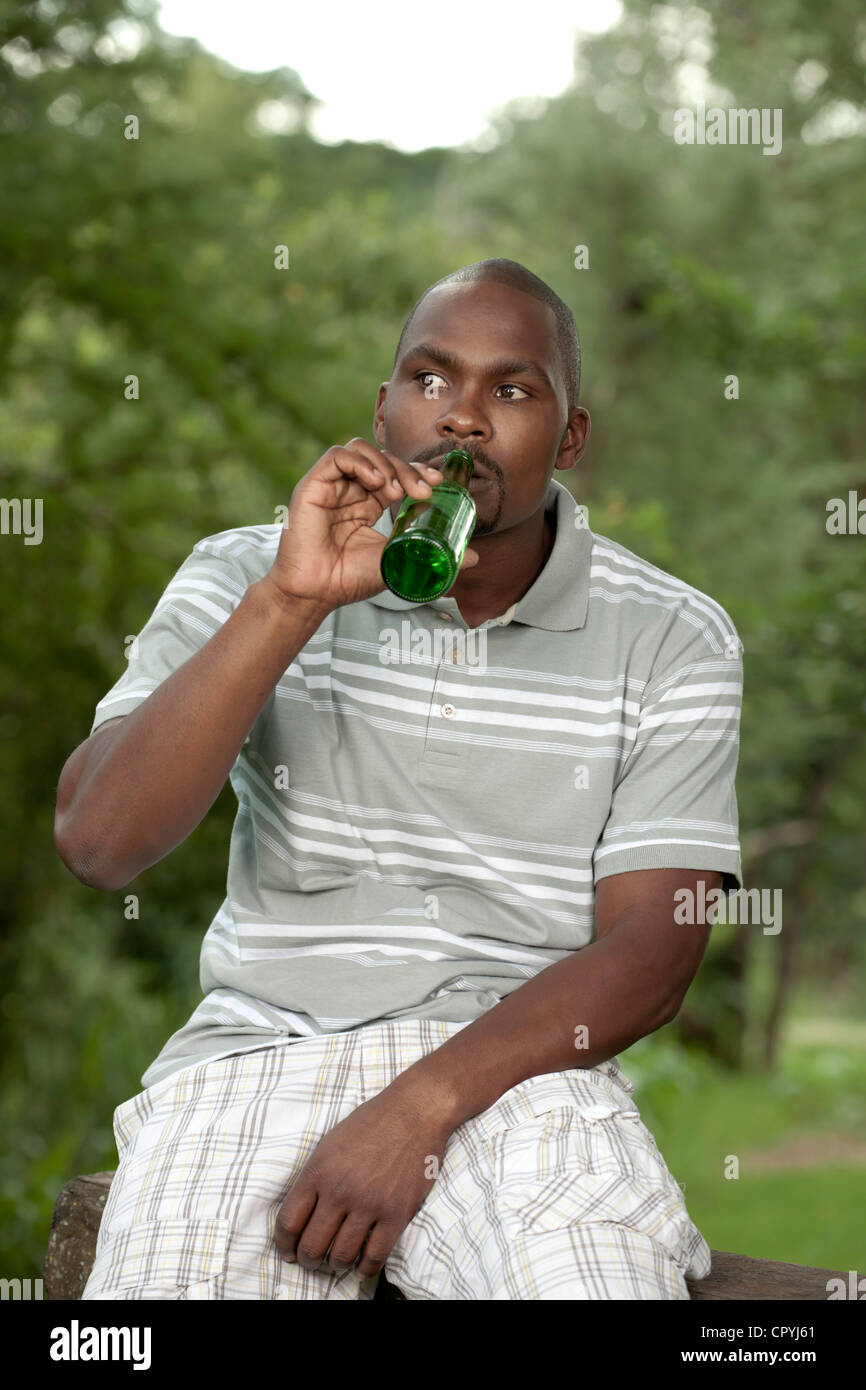 L'uomo africano si siede fuori a bere una birra Foto Stock