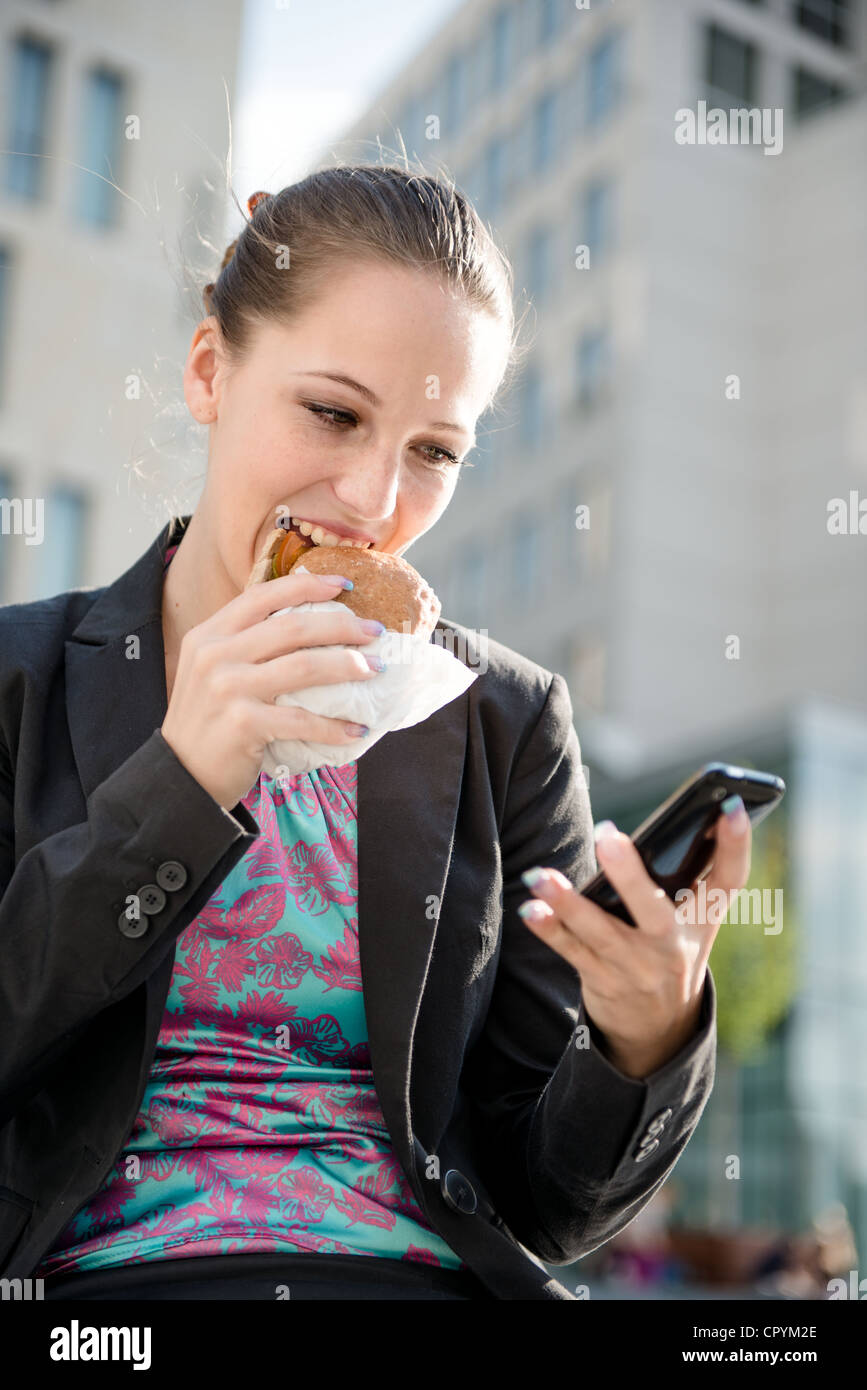 Sorridente business donna mangiare e la lettura messaggio sul telefono cellulare Foto Stock