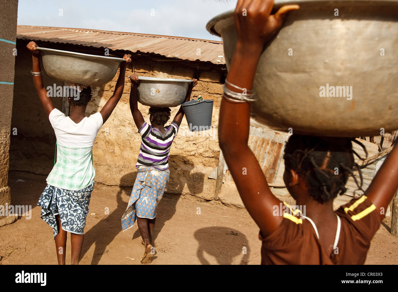 Le ragazze portano ai contenitori di acqua hanno riempito da un bene comune nel villaggio di Kiendi-Walogo, regione di Zanzan, Costa d'Avorio Foto Stock