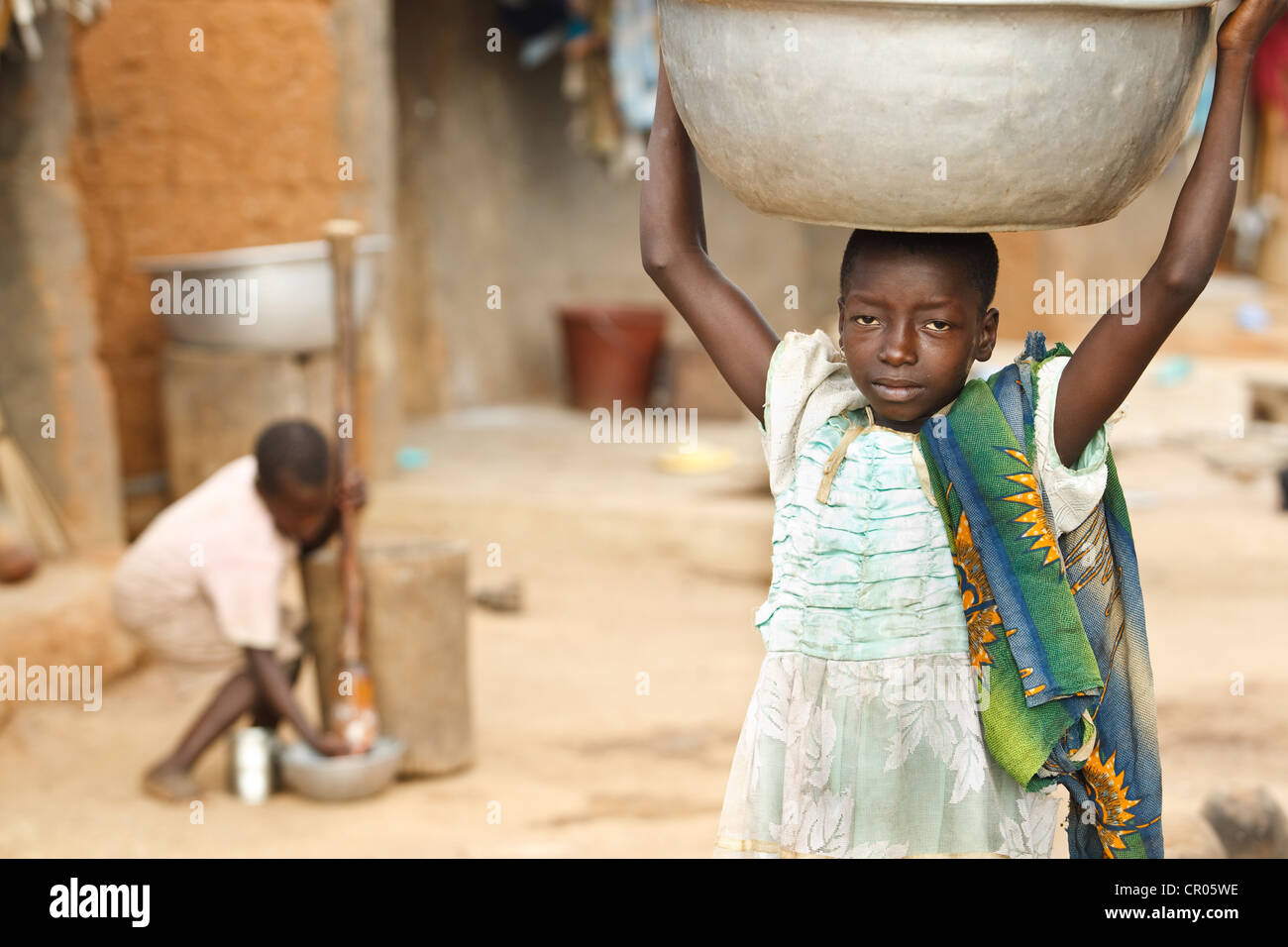 Una ragazza che non andare a scuola porta un vassoio di metallo sul suo capo nel villaggio di Djorbana, regione di Zanzan, Costa d'Avorio Foto Stock