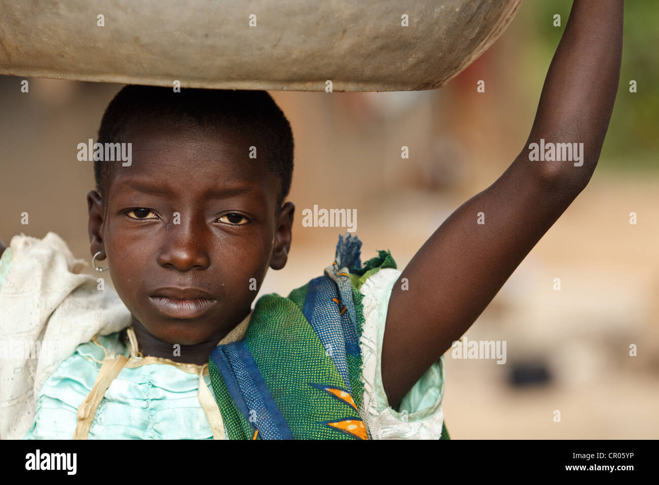 Una ragazza che non andare a scuola porta un vassoio di metallo sul suo capo nel villaggio di Djorbana, regione di Zanzan, Costa d'Avorio Foto Stock