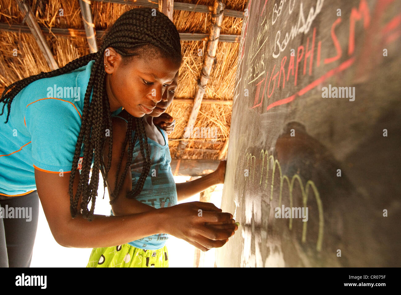 Maestro di volontariato Noufe Mimini Marina, 21, mostra una ragazza come disegnare lettere alla comunità scuola Foto Stock