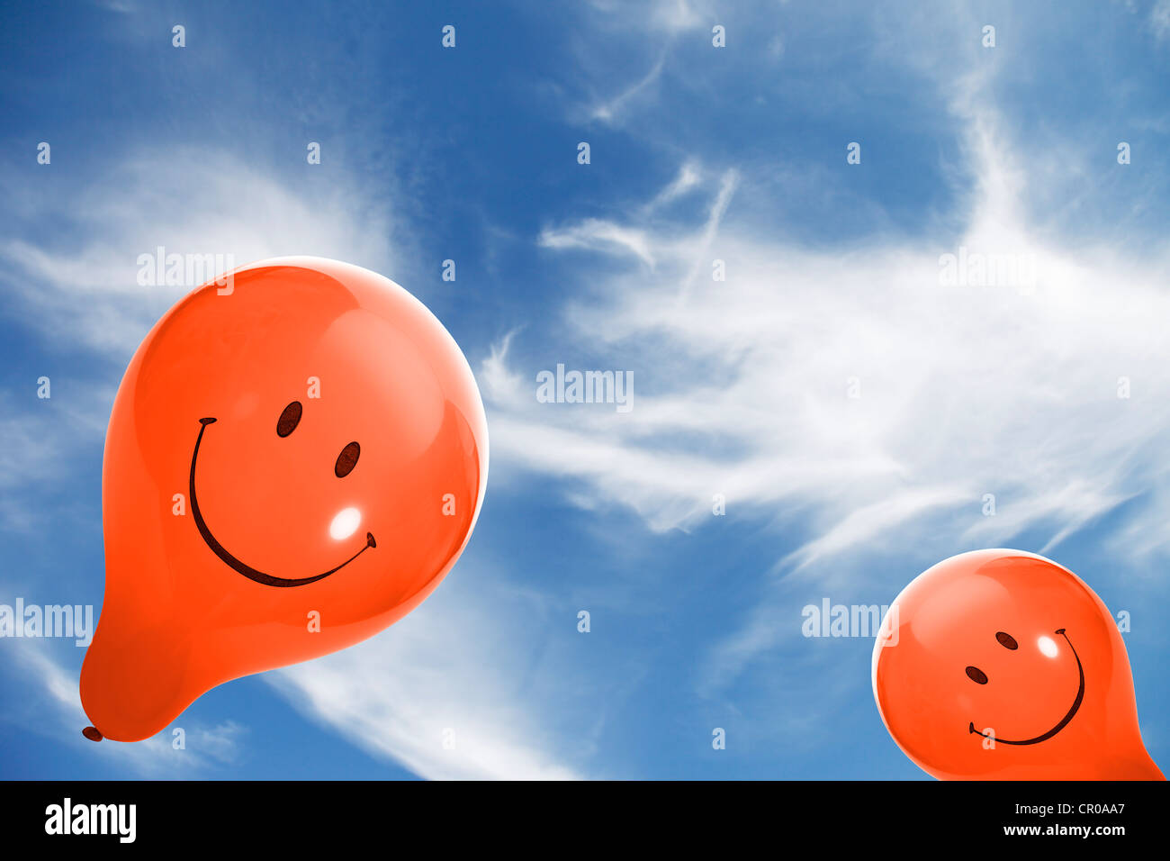 Due arancioni palloncini smiley contro un cielo blu con nuvole Foto Stock
