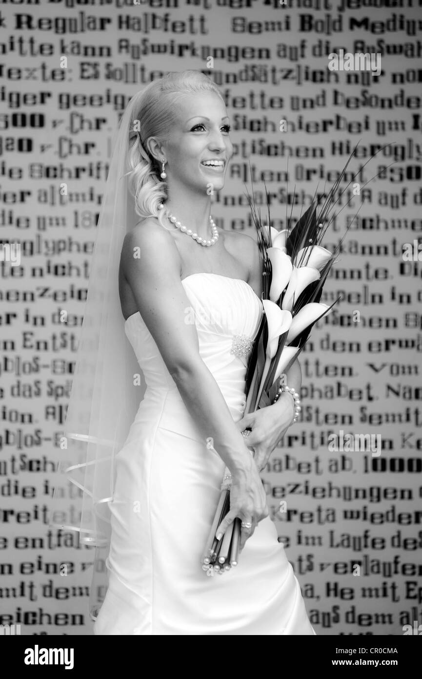 Matrimonio sposa sorridente con bouquet nuziale in piedi di fronte ad una parete con lettere Foto Stock