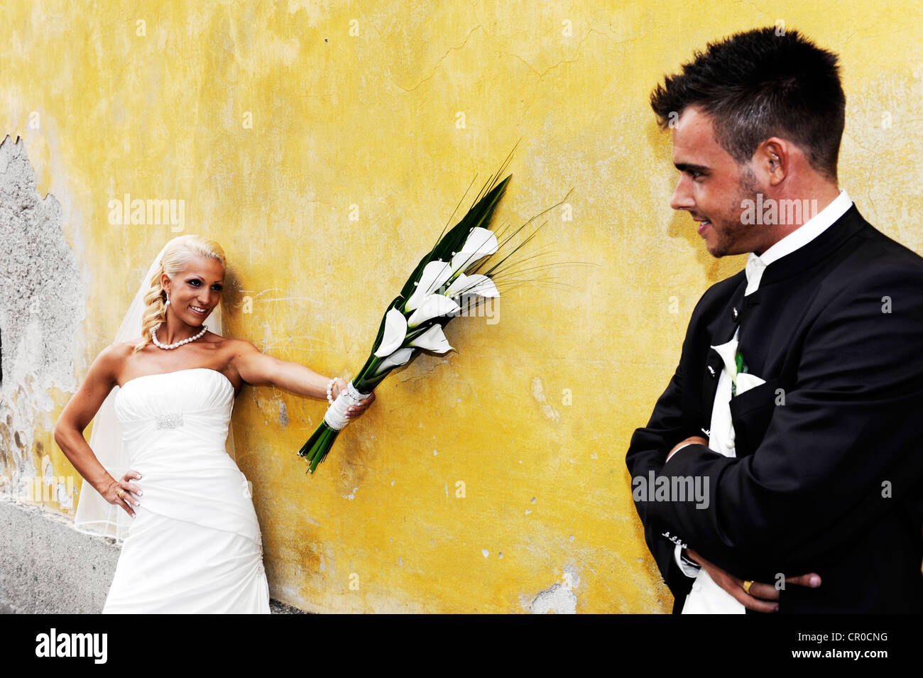 Nozze, ridendo sposa tenendo fuori bouquet della sposa verso lo sposo di fronte ad una parete di colore giallo Foto Stock