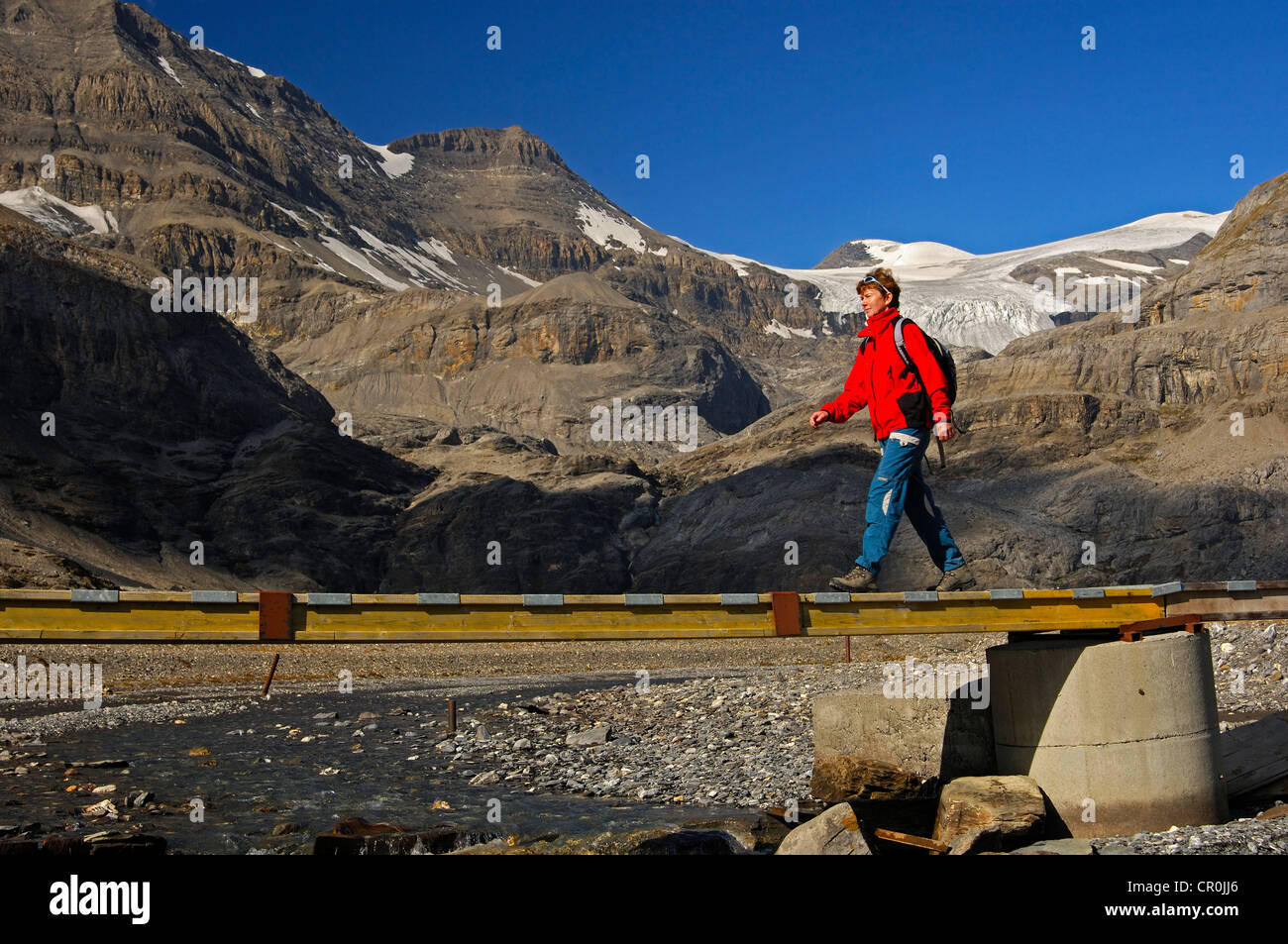 Escursionista attraversando un ponte sul torrente Laemmerenbach, Laemmerboden altopiano di fronte al ghiacciaio Wildstrubel, Alpi bernesi Foto Stock