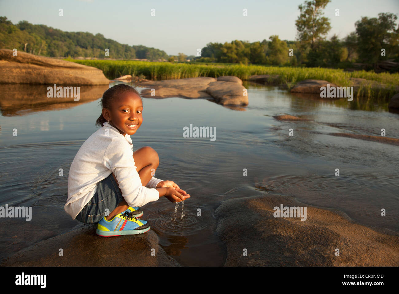 African American Girl scooping acqua dal fiume Foto Stock