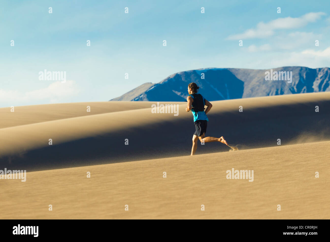 Uomo ispanico in esecuzione sulla duna di sabbia Foto Stock
