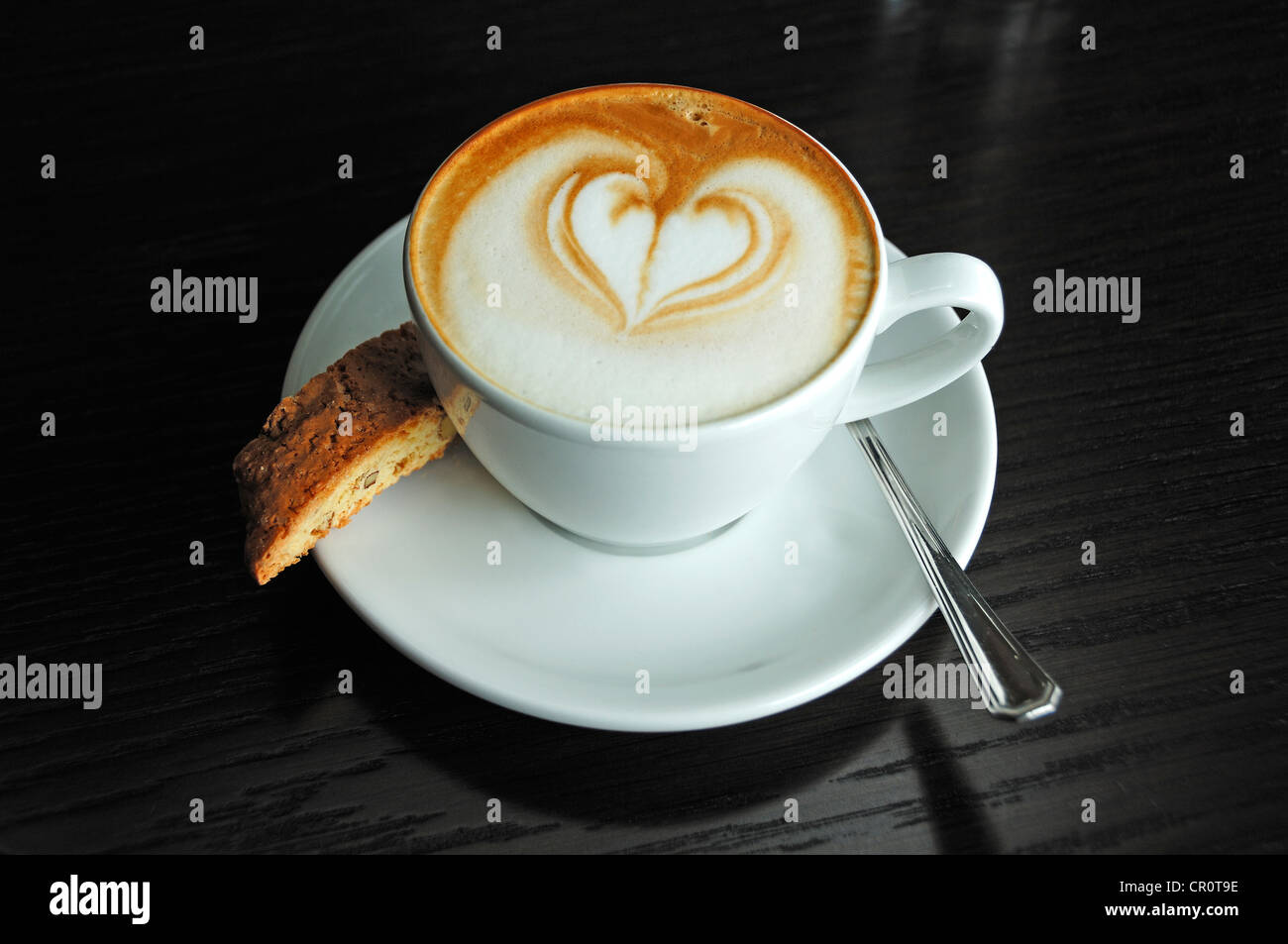 Tazza di cappuccino decorato con un cuore e una biscotti su una tavola nera Foto Stock