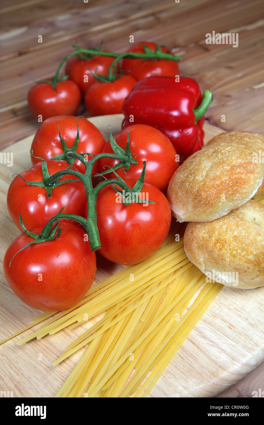 Stile Italiano ingredienti compresi i pomodori, non cotti linguine, cipolla e aglio con cena rotoli su un sfondo di legno - con Foto Stock