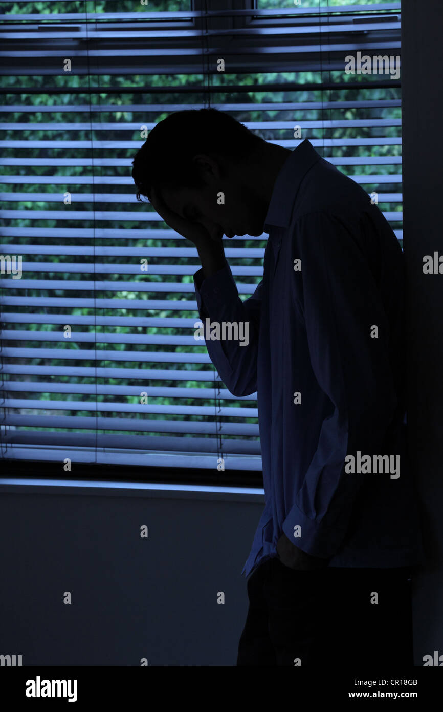 Silhouette di un giovane maschio appoggiata ad una parete per mezzo di una finestra. Foto Stock
