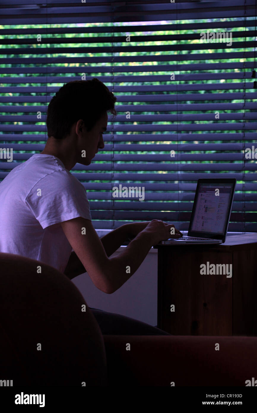 Giovane maschio seduto in una stanza buia con un computer portatile. Foto Stock