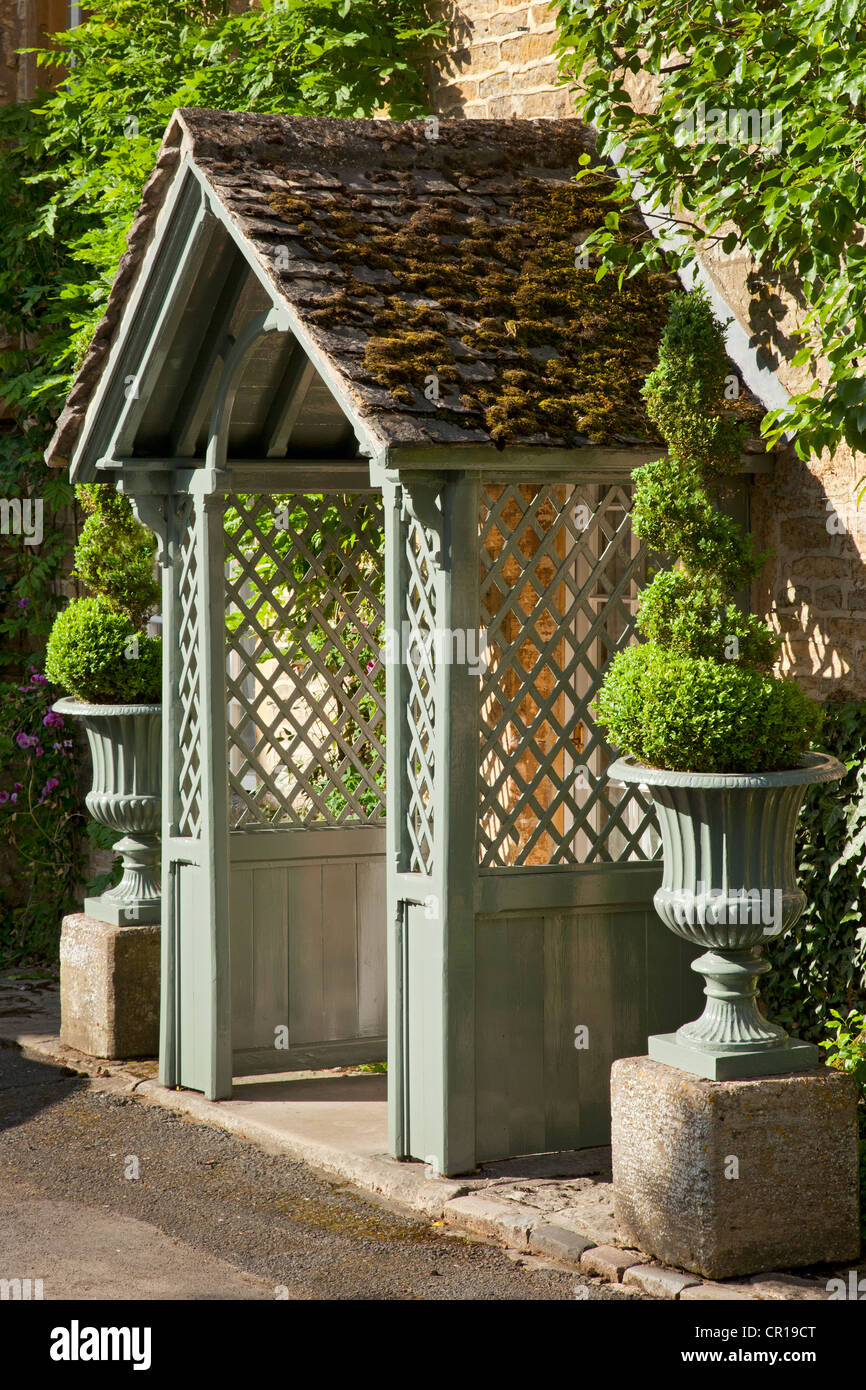 Veranda in legno con lati di reticolo di Cotswold cottage affiancato da casella Topiaria da a spirale in urne di pietra, Inghilterra Foto Stock