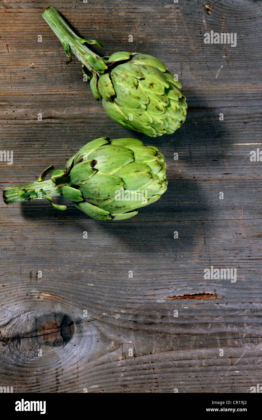 Due i carciofi (Cynara cardunculus) su un rustico di una superficie di legno Foto Stock